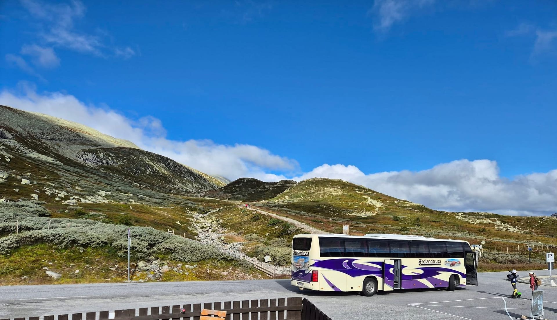 Frolandsruta-bussen i krem og lilla parkert på fjellet under blå himmel