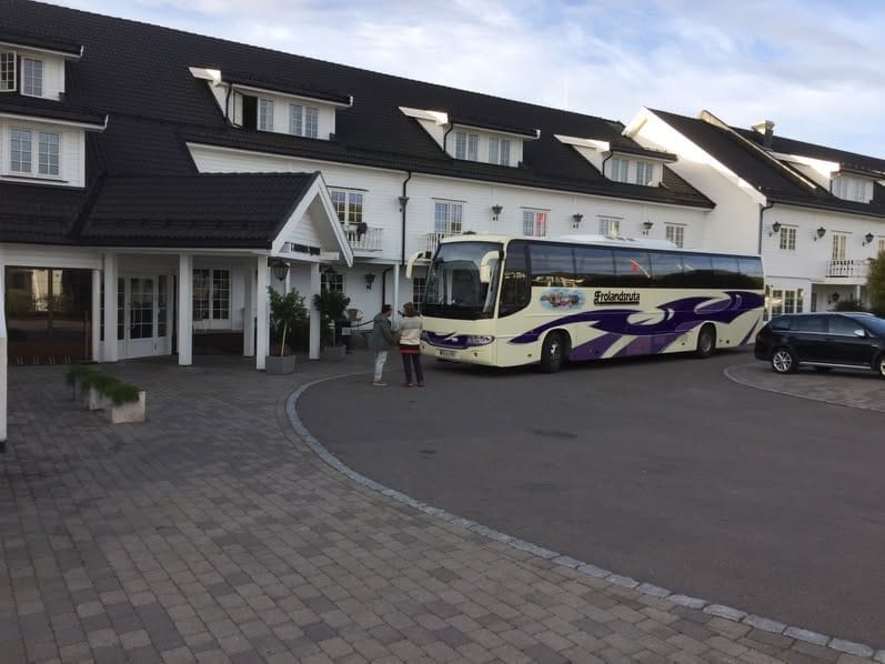 Bussen parkert foran et hvitt hotell med reisende på vei inn